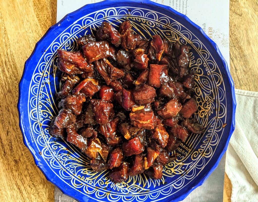 Cubed meat marinating for Beef Lok Lak in a large vibrant, blue and white bowl.