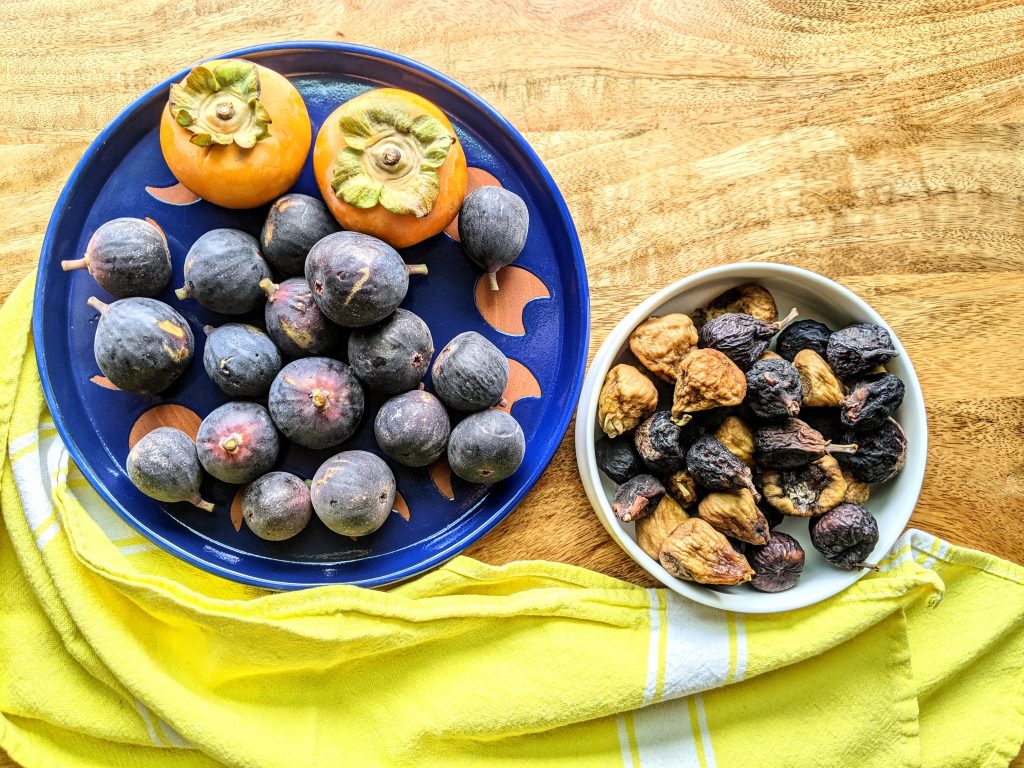 A plate of fresh Mission figs and two kumquats and a small bowl of sun-dried mixed figs.