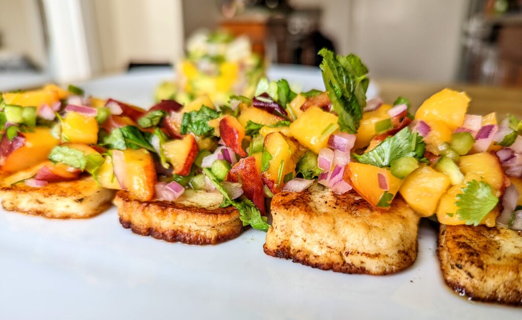 A closeup of a few pieces of grilled halloumi topped with a generous amount of peach salsa.