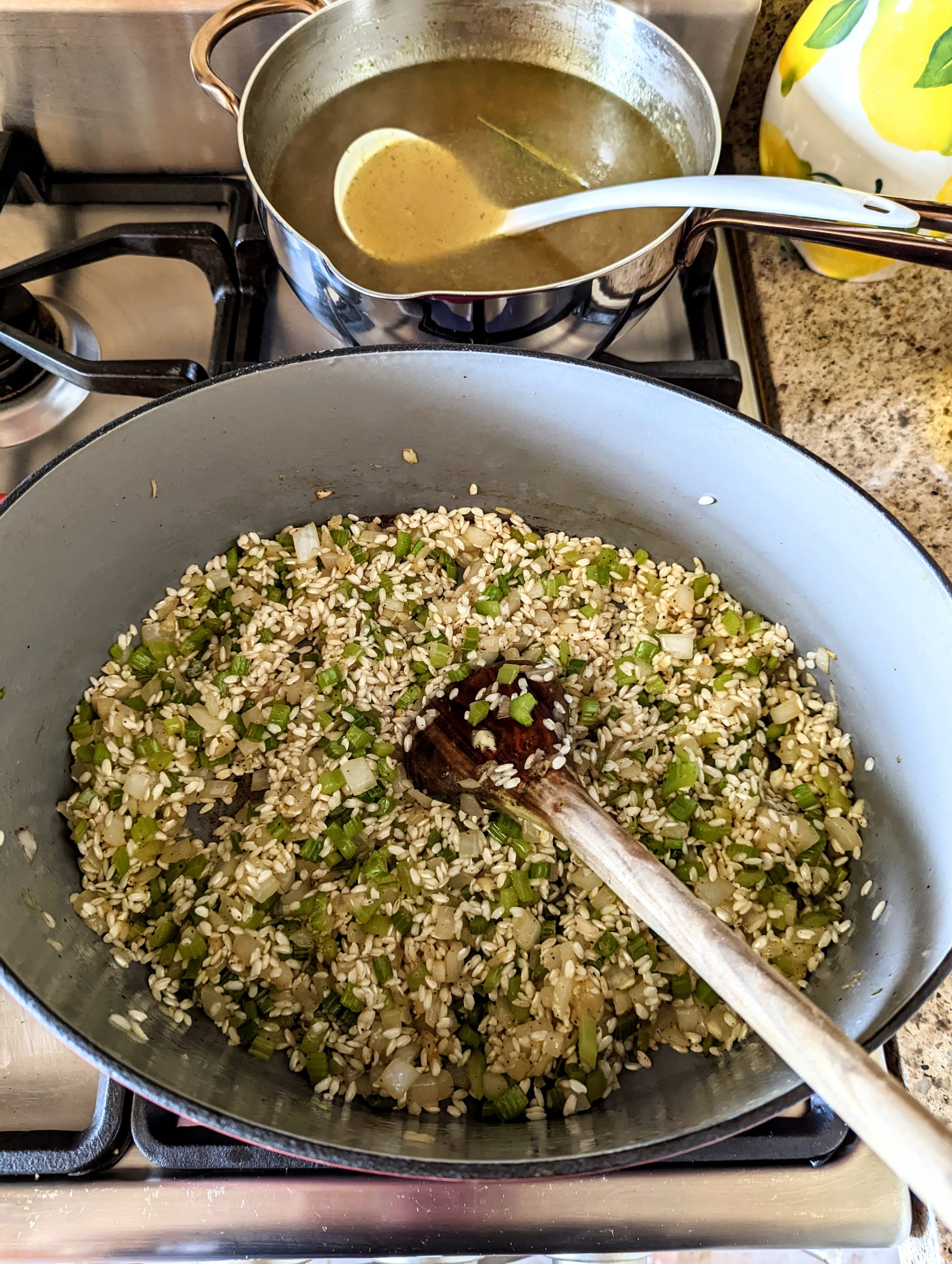 Toasting the arborio rice in the same Dutch oven with the celery and onion. A pot of hot chicken stock is warming on the burner behind it.