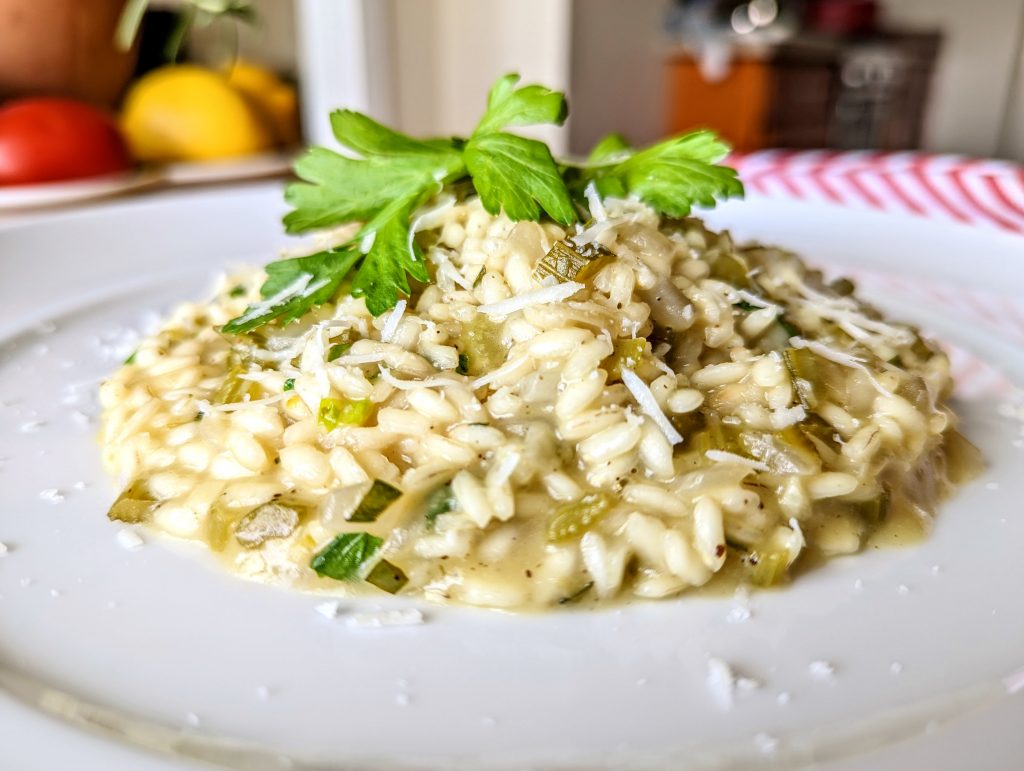 A table-side closeup of the celery and tarragon risotto, topped with celery leaves and Pecorino Romano cheese.
