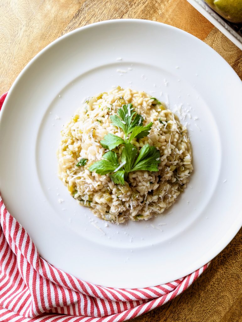A large white plate of Celery and Tarragon Risotto, garnished with celery leaves and Pecorino Romano.