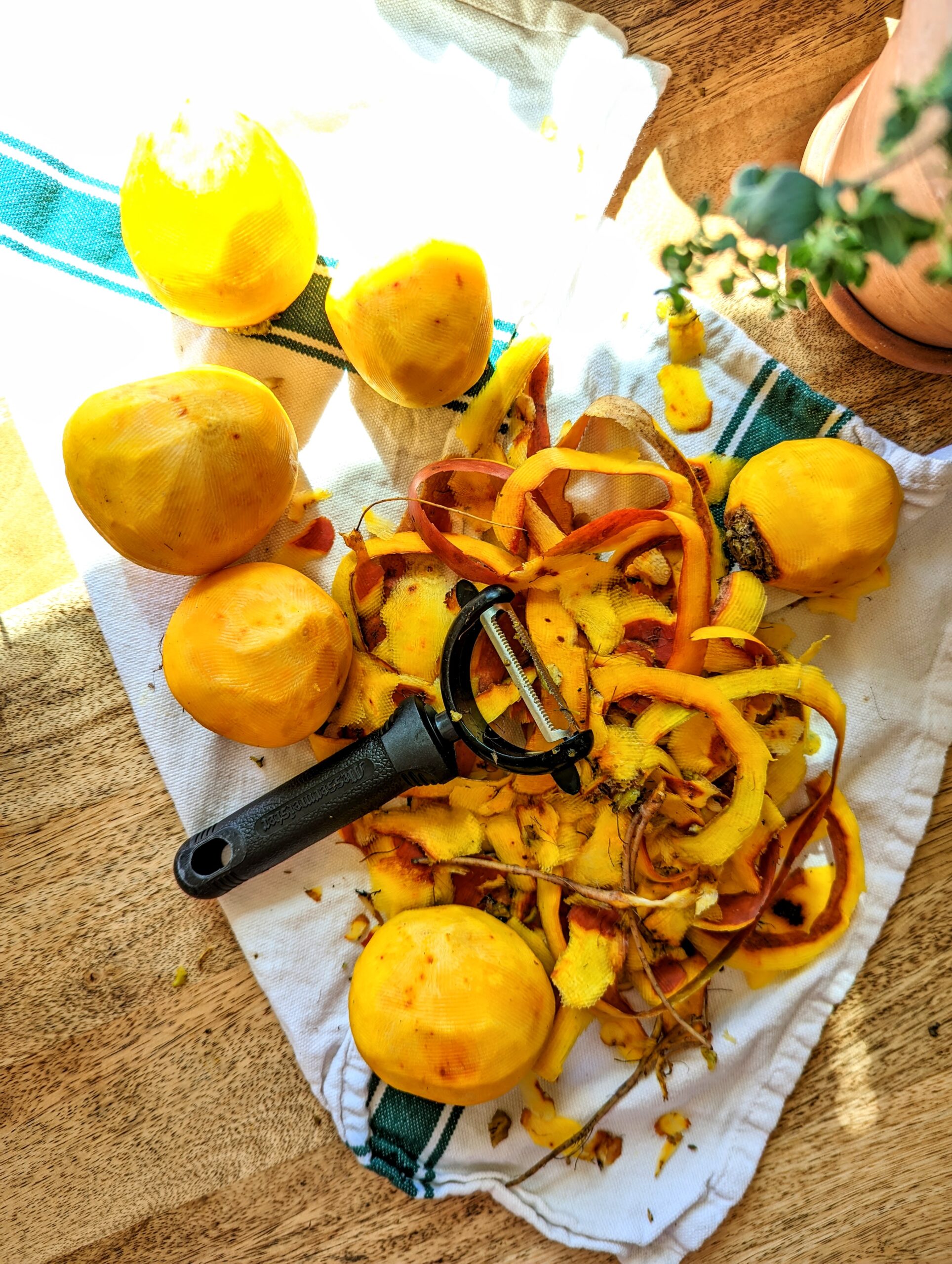 Six freshly peeled golden beets resting on a white and green kitchen towel. All of the beet shavings are in a pile in the middle of the kitchen towel.