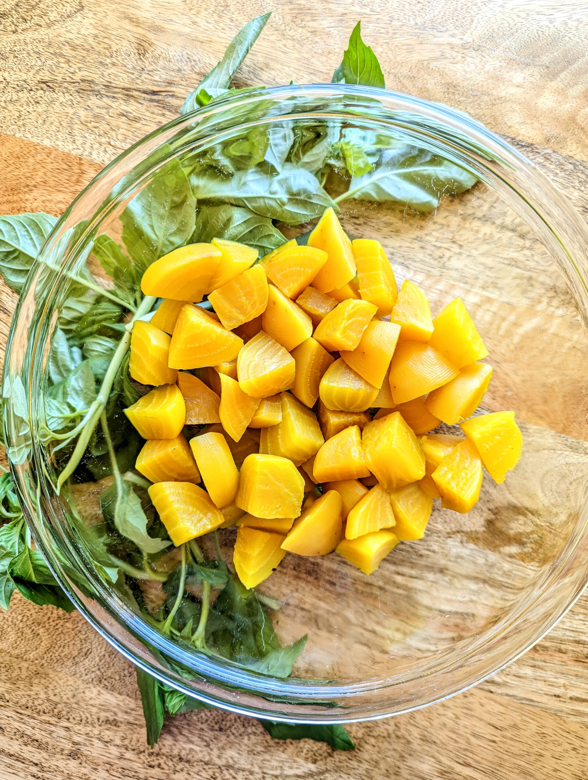 A bowl of steamed and chilled golden beets with fresh basil.