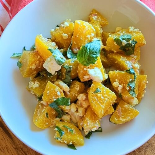 A white bowl of golden beet salad with feta and basil. A red kitchen towel drapes the top if of the bowl.