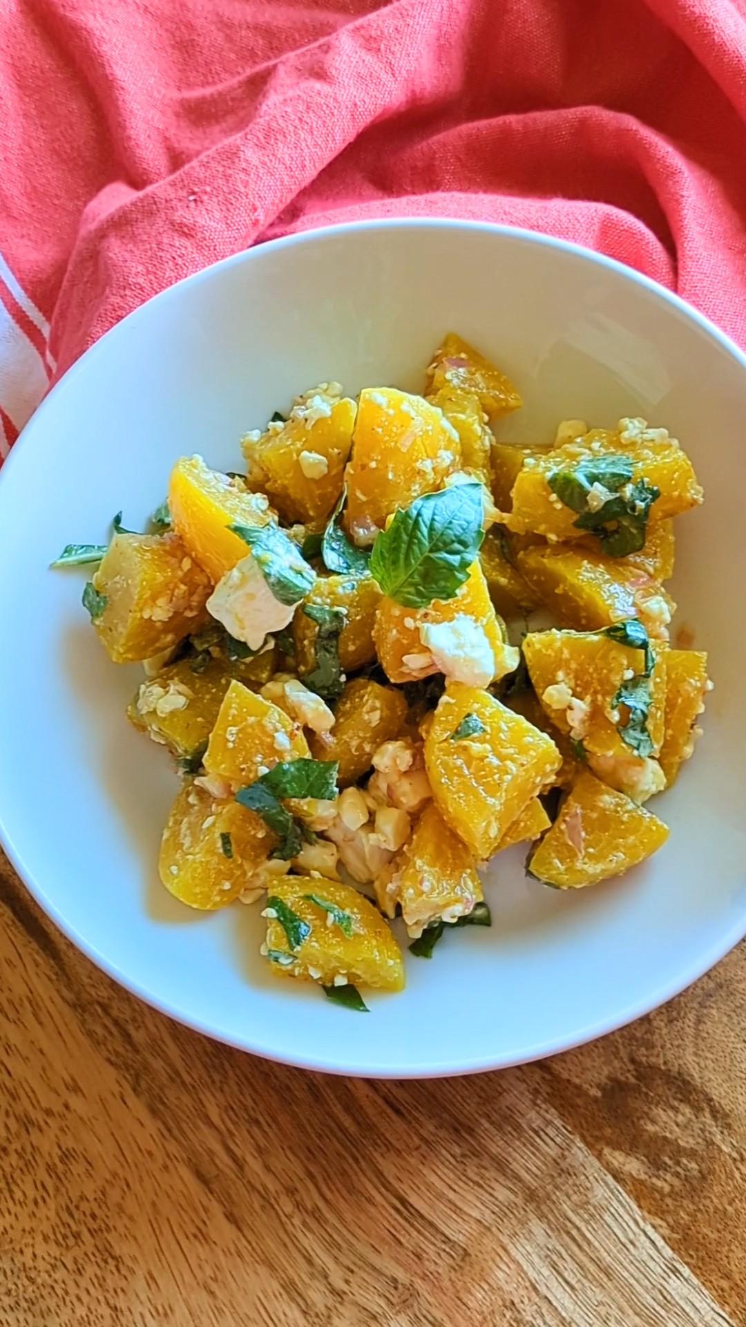 A white bowl of golden beet salad with feta and basil. A red kitchen towel drapes the top if of the bowl.