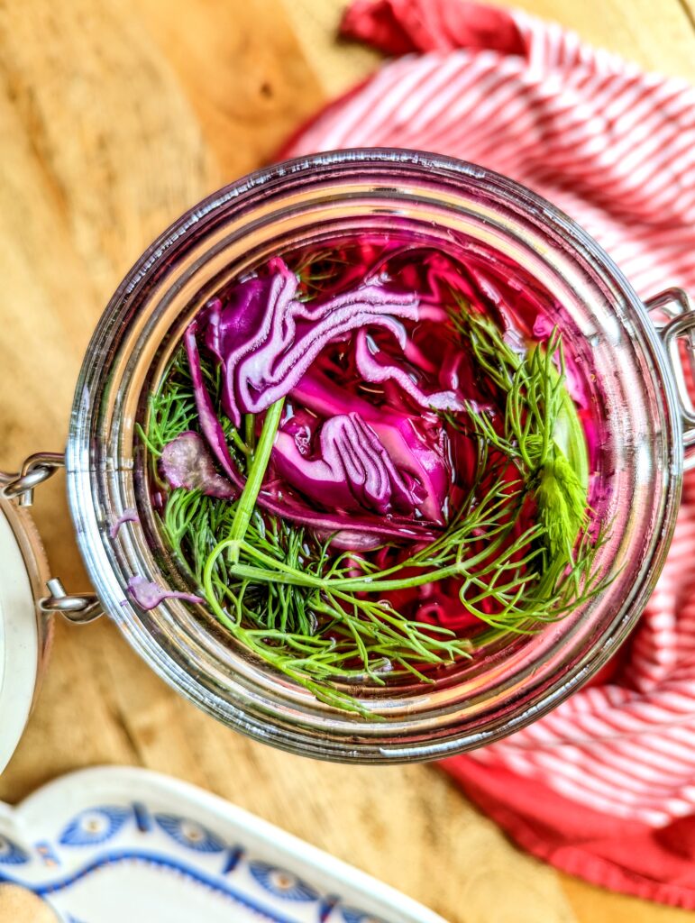 An open jar of red cabbage, dill, and brine all ready for the fridge.