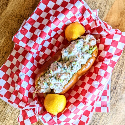 An aerial view of a lobster roll dupe. The langostino roll is plated in vintage red and white checkered diner platters.