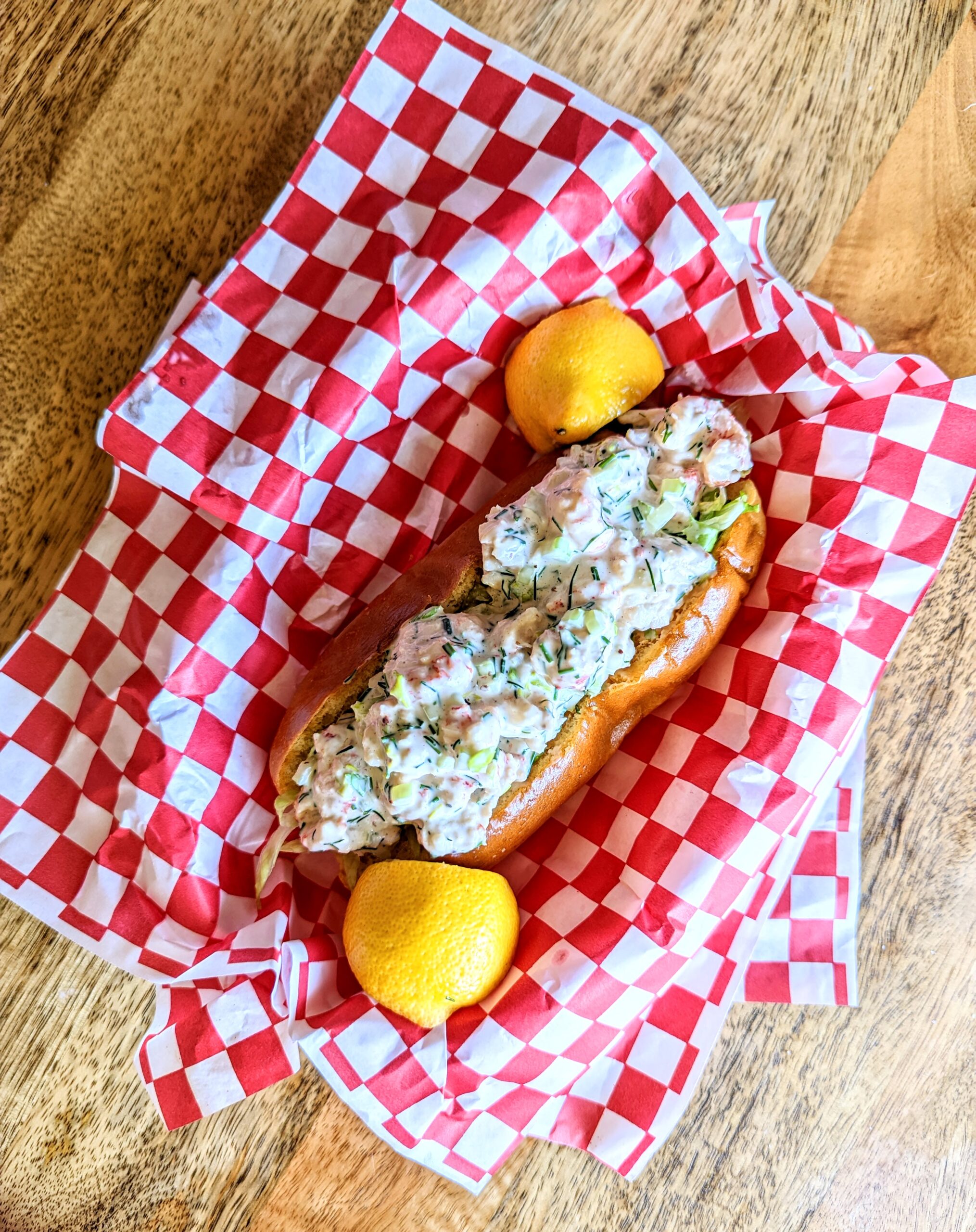 An aerial view of a lobster roll dupe. The langostino roll is plated in vintage red and white checkered diner platters.