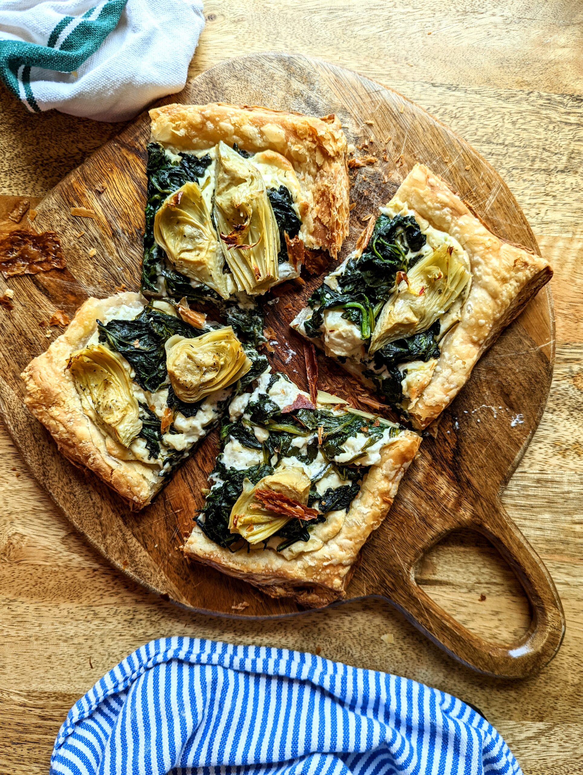 A spinach and artichoke tart on top of a circular wooden cutting board.