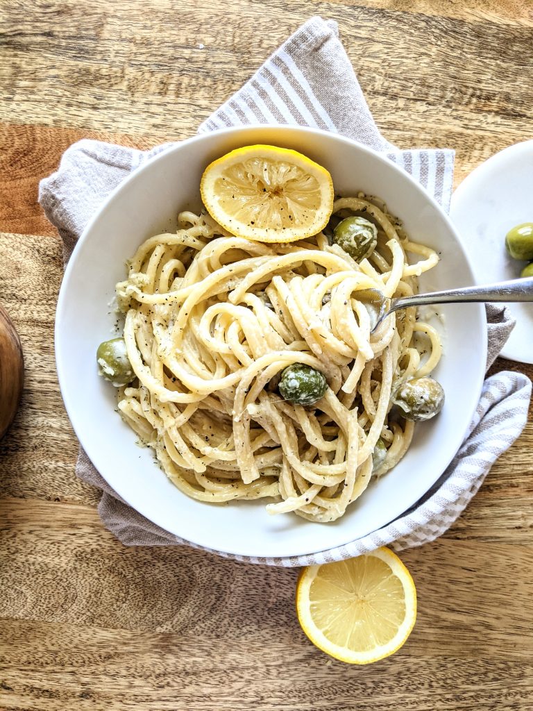 A bowl of bucatini pasta with green Castelvetrano olives and a squeezed half of a lemon.