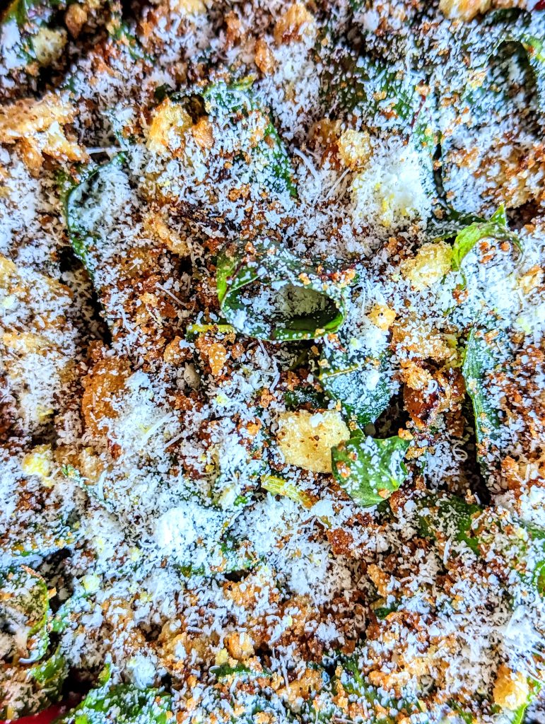 A closeup of green Swiss Chard Salad with golden breadcrumbs, and white pecorino snow.