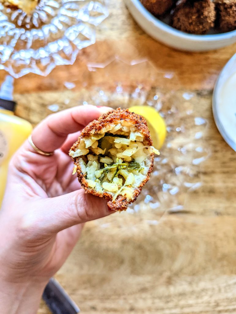 A hand holding an arancini ball after a bite has been taken out of it. The inside is full of zucchini risotto and melted cheese.