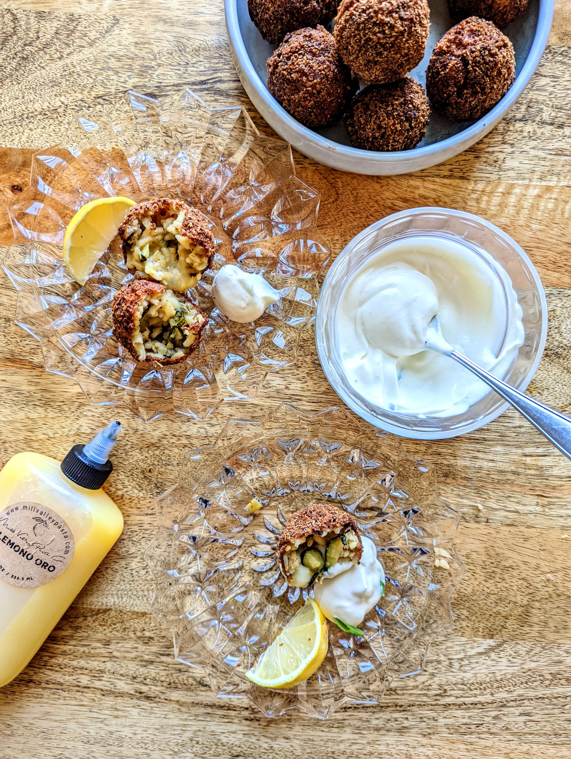 Crunchy and creamy arancini balls full of zucchini and melted cheese. A small bowl of preserved lemon aioli and a bottle or preserved lemon puree can be seen in the photo.