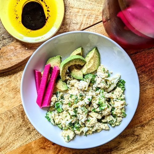 A colorful plate of pinks and greens. Kale and egg scramble with sliced avocado and pink pickled turnips.