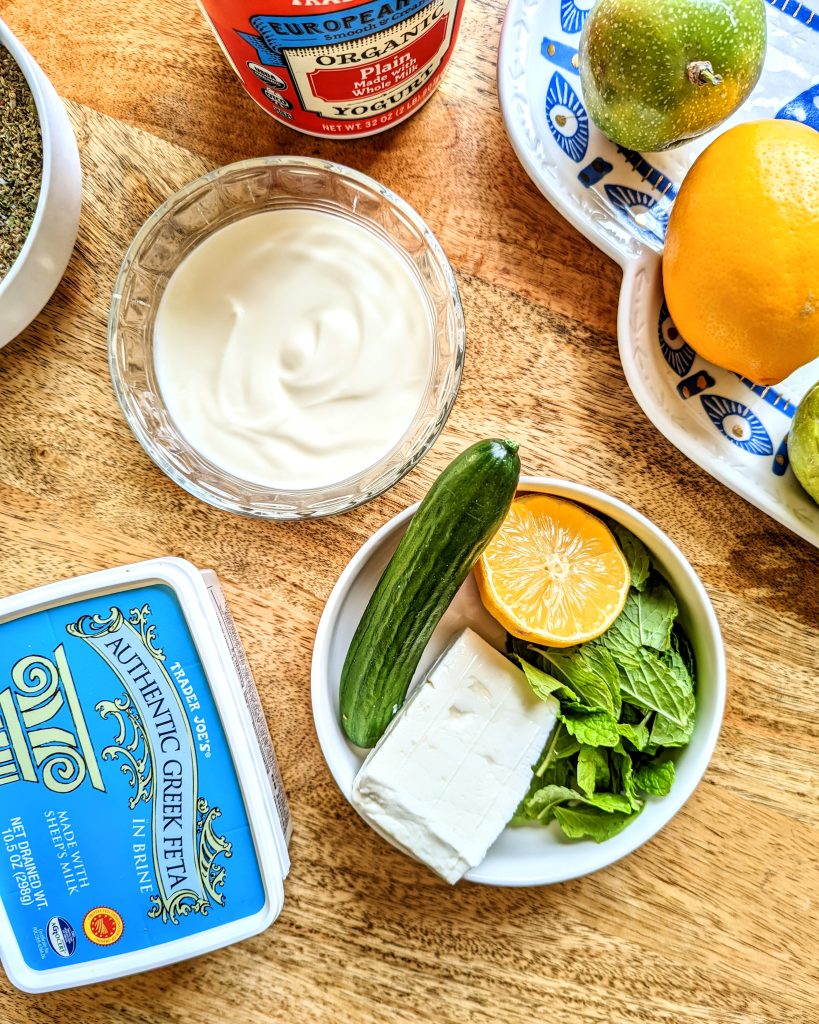 A bowl of yogurt, a chunk of feta, half a lemon, a Persian cucumber, and a handful of fresh mint.
