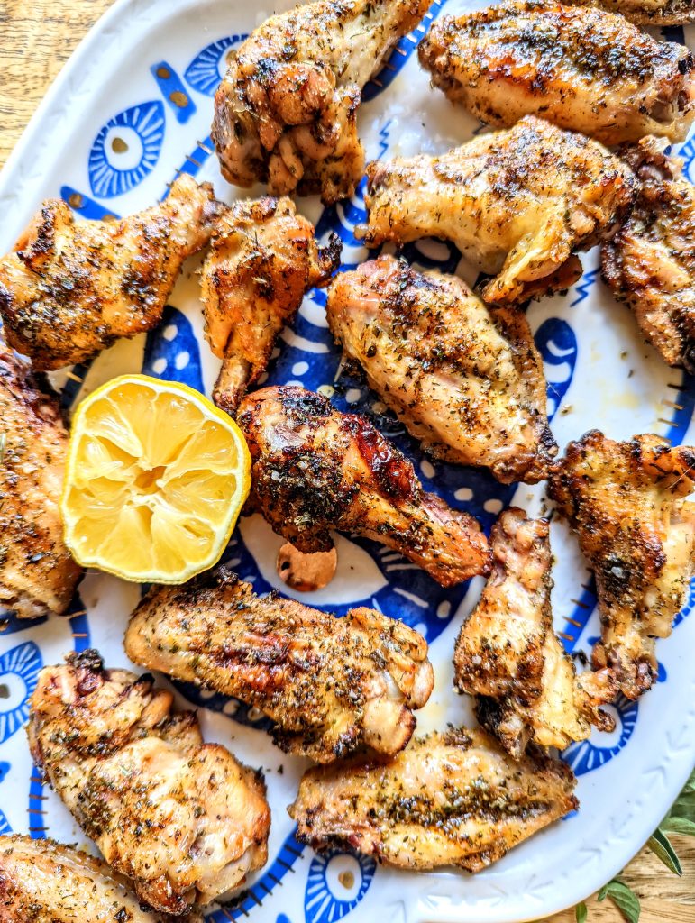 An aerial zoomed in shot of a platter of chicken wings. A freshly squeezed half of a lemon sits in the middle of the platter.