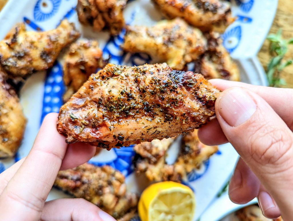 Two hands holding each end of a chicken wing flat. A platter of chicken wings and fresh lemon wedges can be seen in the background.