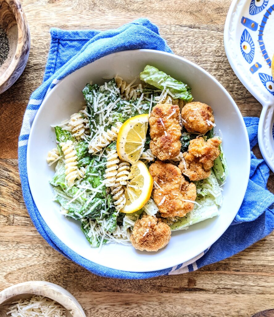 A Chicken Caesar Pasta Salad. The white bowl is wrapped loosely in a blue and white kitchen towel.