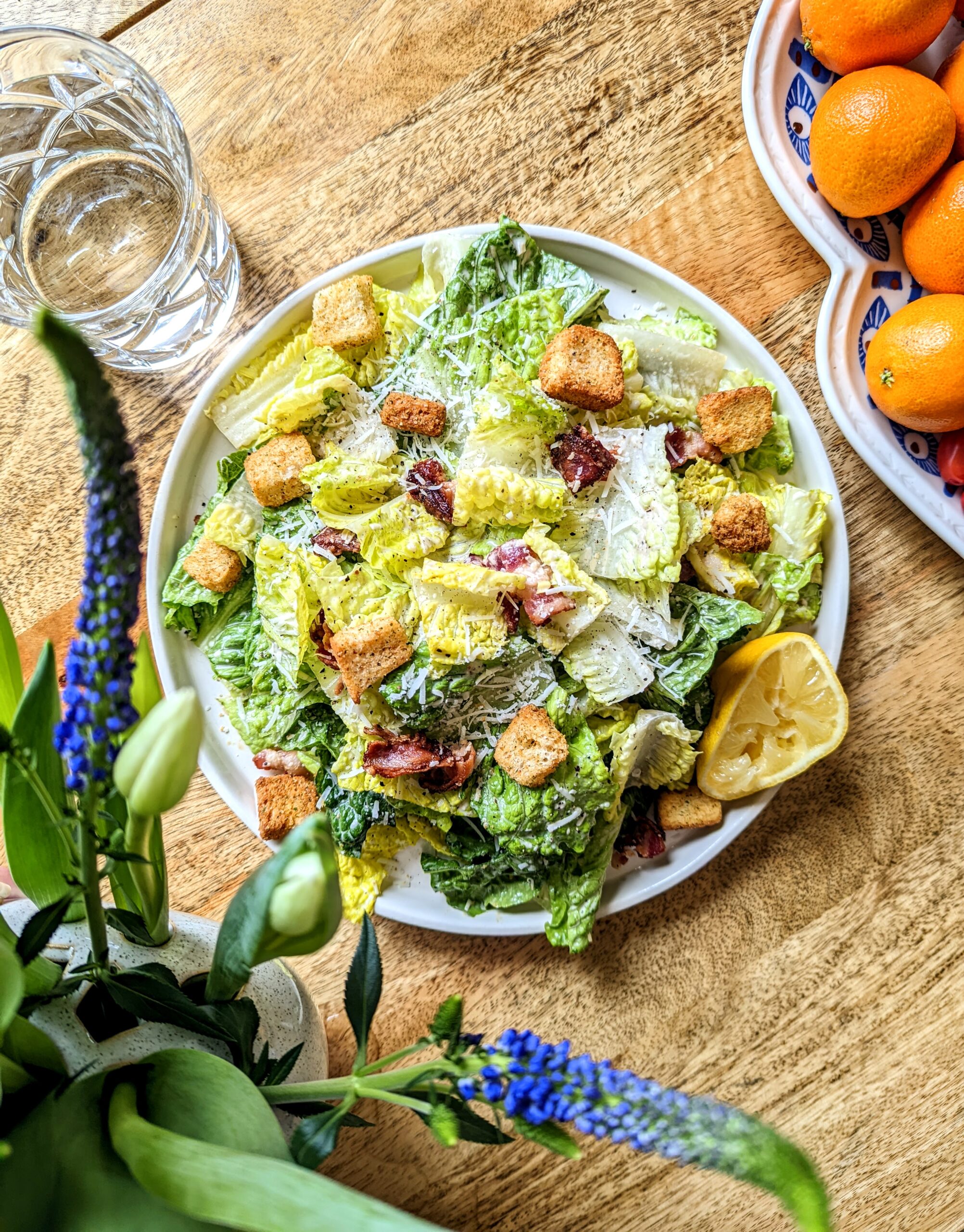 A plate of classic caesar salad with large crisp pieces of bacon, homemad croutons, and a lemon half.