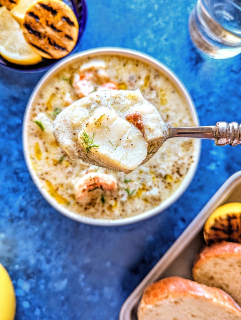 A spoonful of Seafood Chowder showcasing scallops, bacon, shrimp, and grilled lemon.