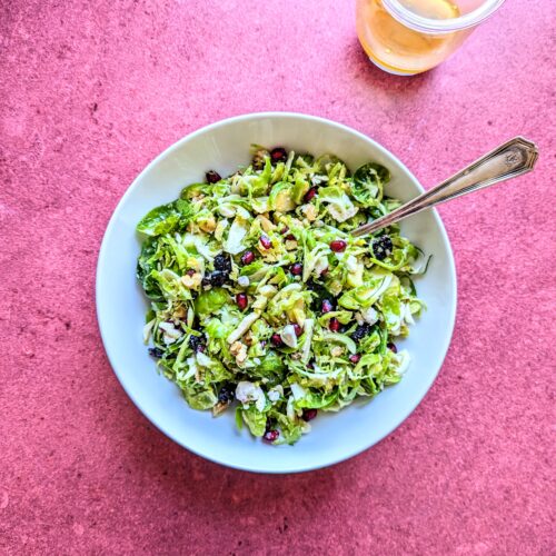 A bowl of Shaved Brussels Sprouts Salad over a deep red backdrop.