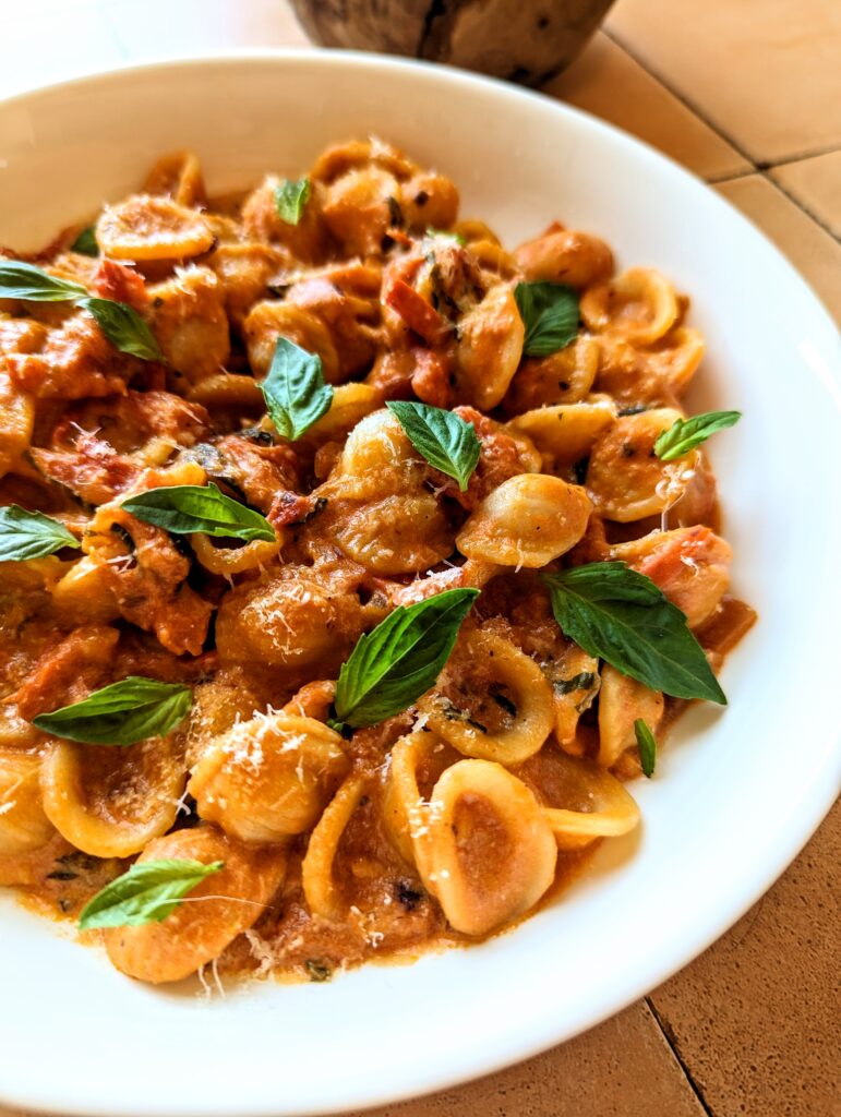 A table-side view of Tomato Basil Orecchiette. A red based sauce, topper with green basil leaves, and finely grated white cheese.