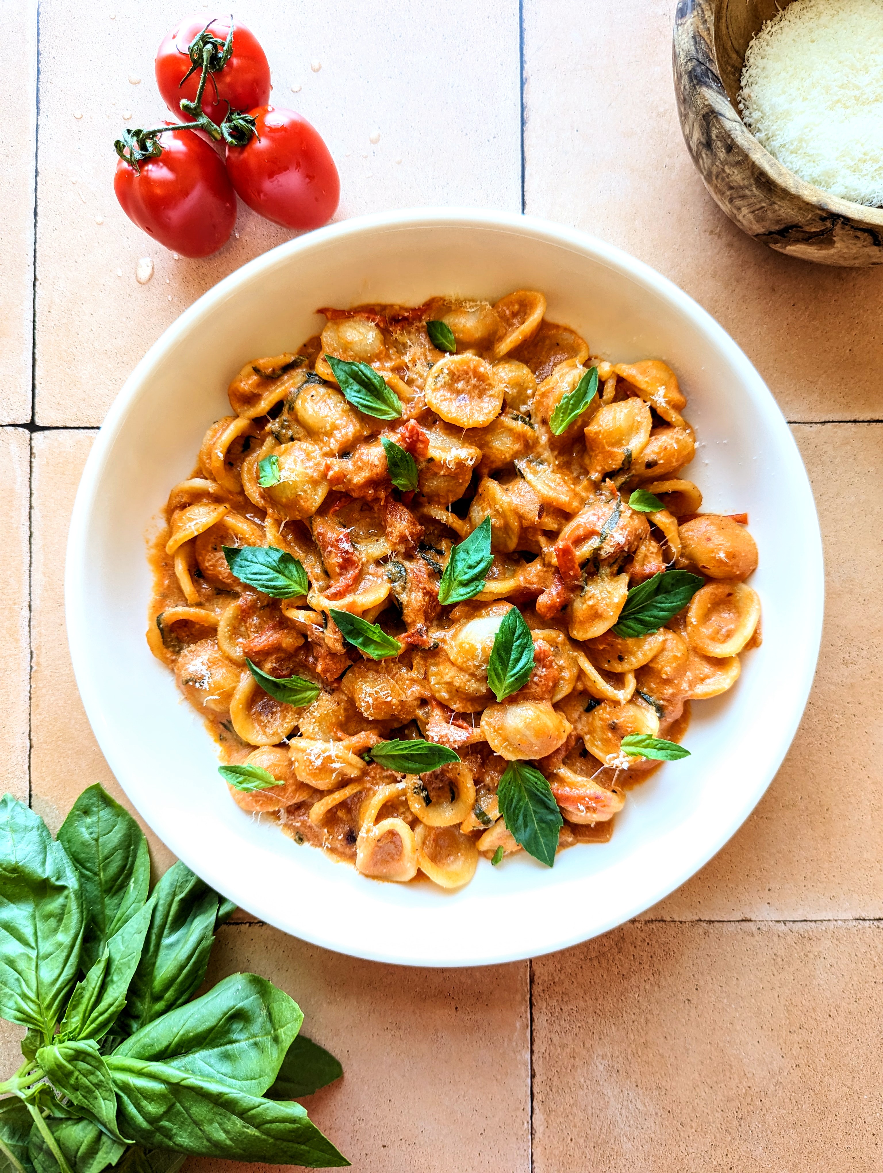 A bowl of creamy tomato basil pasta garnished with small, green, fresh basil leaves.