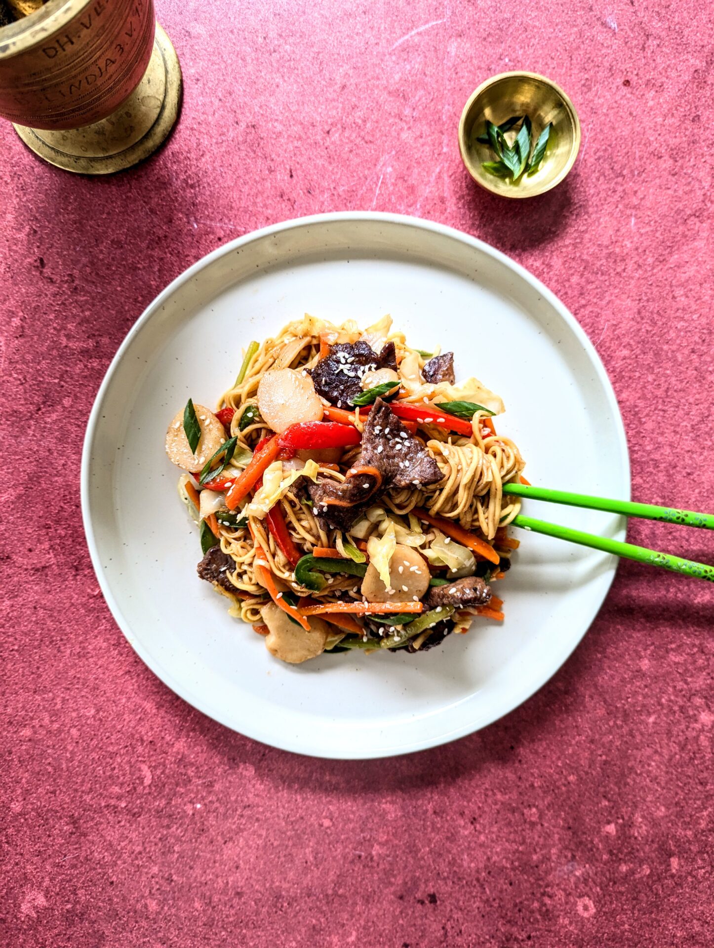 A plate of beef chow mein with the noodles wrapped around the chop sticks.