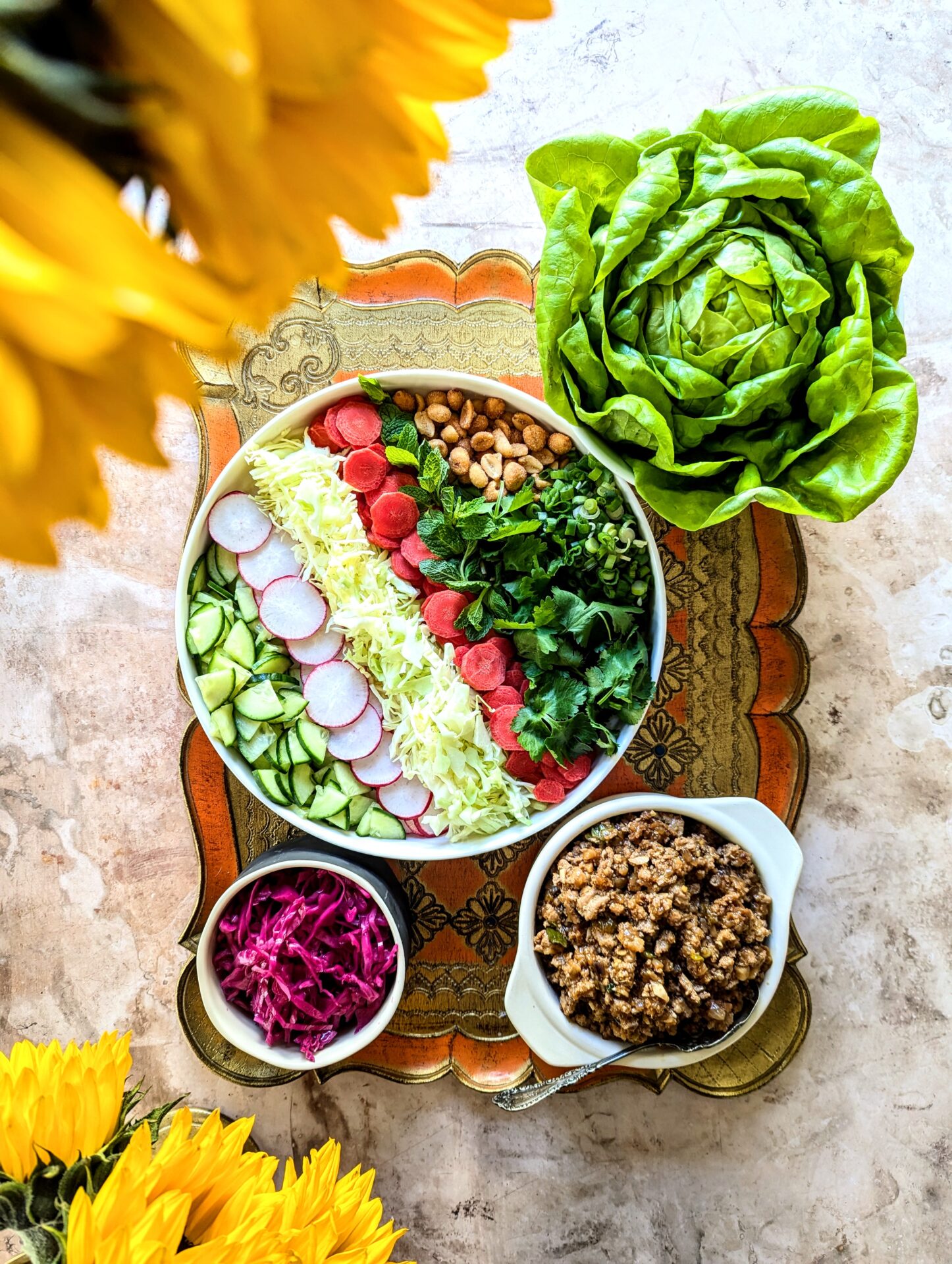 A tray full of an assortment of chopped vegetables, ground chicken filling, a head of butter lettuce, and pickled red cabbage.