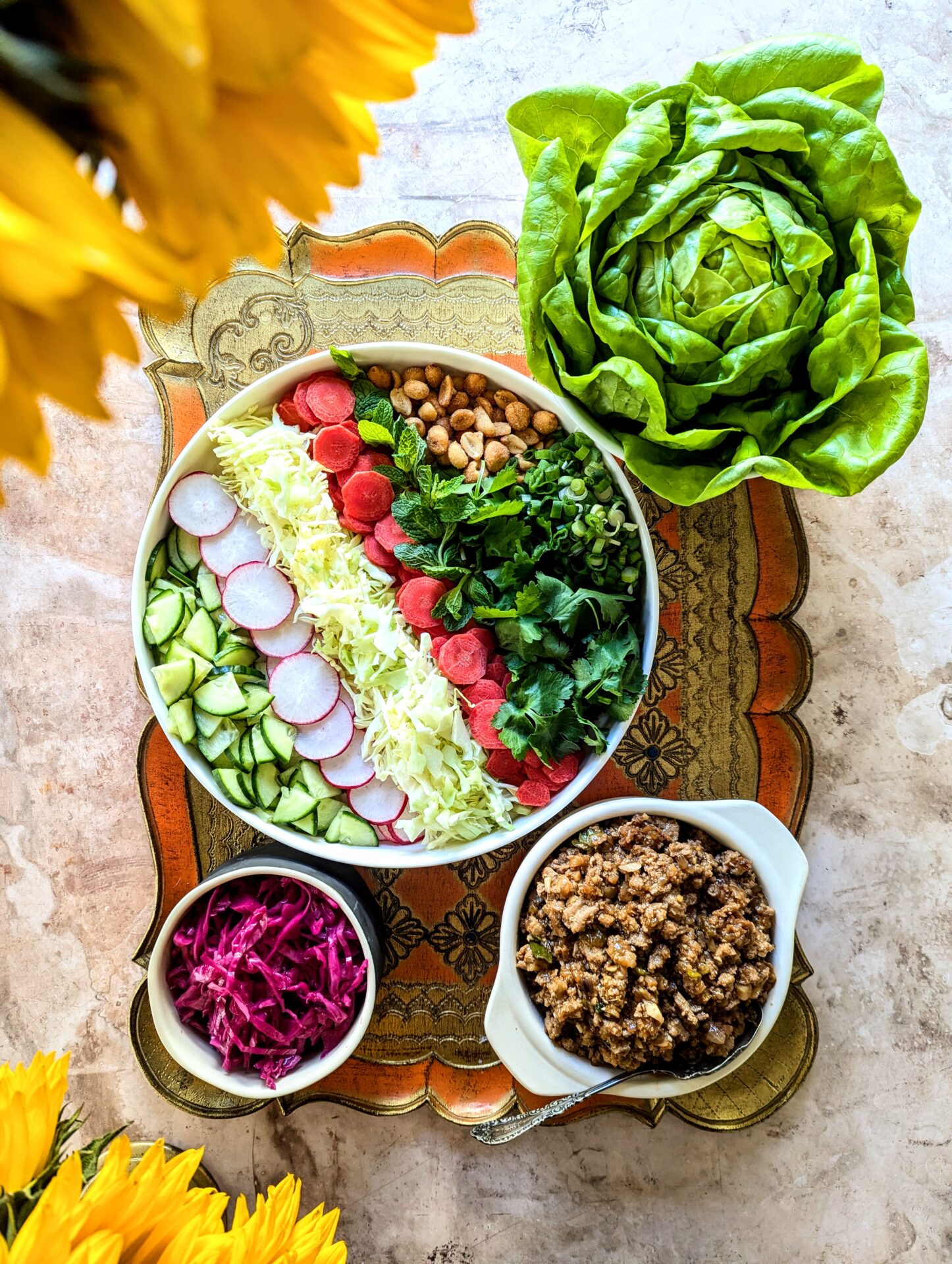 A tray full of an assortment of chopped vegetables, ground chicken filling, a head of butter lettuce, and pickled red cabbage.